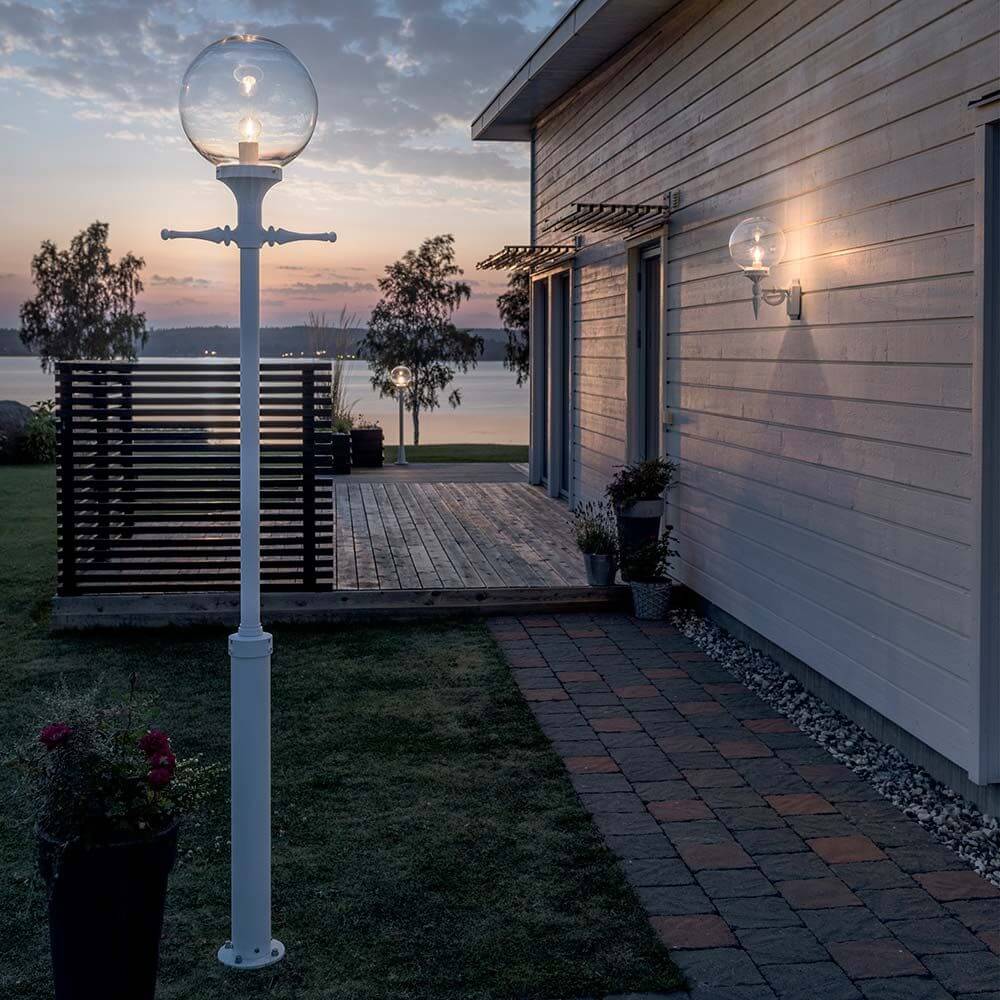 Orion Standleuchte Weiß, klares Acrylglas im Garten bei Dämmerung, moderne Beleuchtung für Außenbereiche.