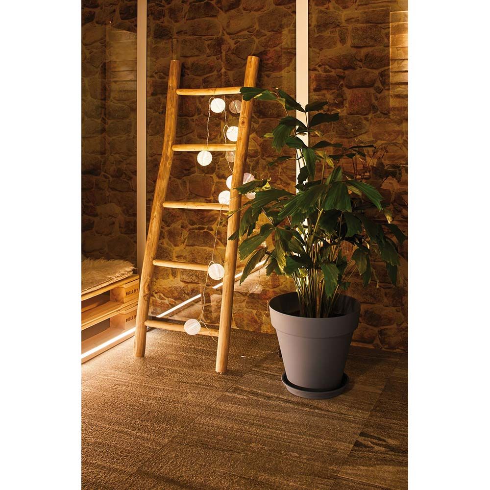 Akku LED Lampionkette IP44 leuchtet warmweiß an einer Holzleiter neben einem grünen Pflanzenkübel.