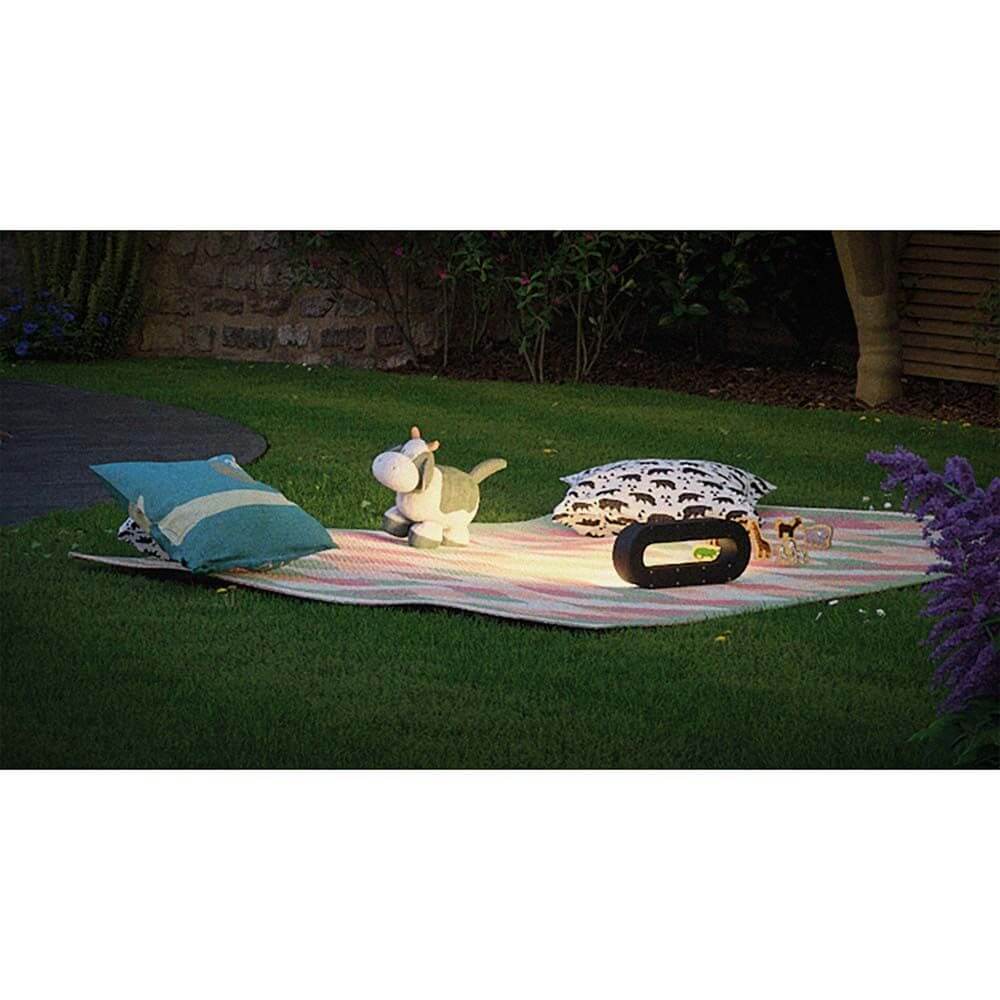 LED Akkuleuchte Moval IP44 370lm 3000K USB auf einer Decke im Garten mit Kissen und Dekorationsobjekten.