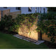 LED Plug & Shine Bodenaufbauleuchte 115° IP67 3000K Anthrazit beleuchtet eine Gartenmauer mit Pflanzen.