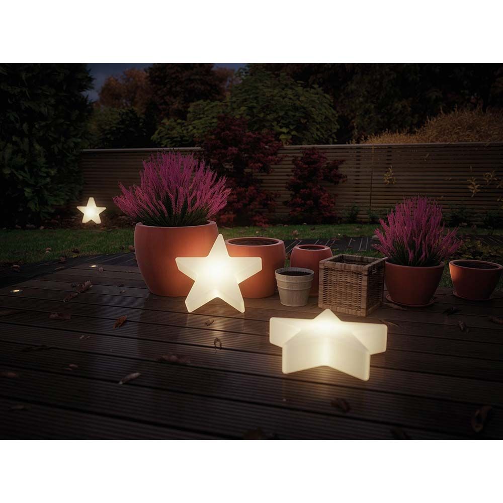 Beleuchtete Stern-Lichtobjekte im Garten auf einer Terrasse, umgeben von blühenden Pflanzkübeln.