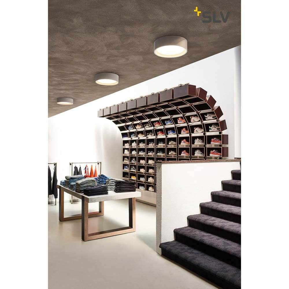 Plastra LED Deckenleuchte Weiß 3000K in einem modernen Geschäft mit stylischen Regalen und Treppen.