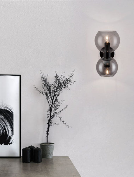 Applique Palmer Ø 13 cm E14 à 2 lampes, noire, fumée, sur un mur avec des décorations modernes.