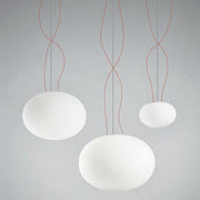 Panzeri Gilbert Glas Pendelleuchte in modernem Design, mit drei hängenden, weißen Glaskugeln und roten Kabeln.