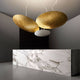 Moderne Panzeri Gong LED-Pendelleuchte mit goldenen Scheiben über einer Marmor-Theke in elegantem Raumdesign.