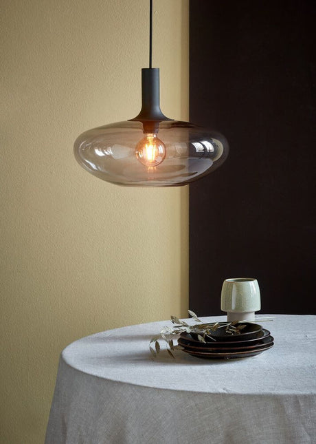 Pendelleuchte Alton 35 aus rauchfarbenem Glas, elegante runde Form und warmes Licht auf einem Tisch.