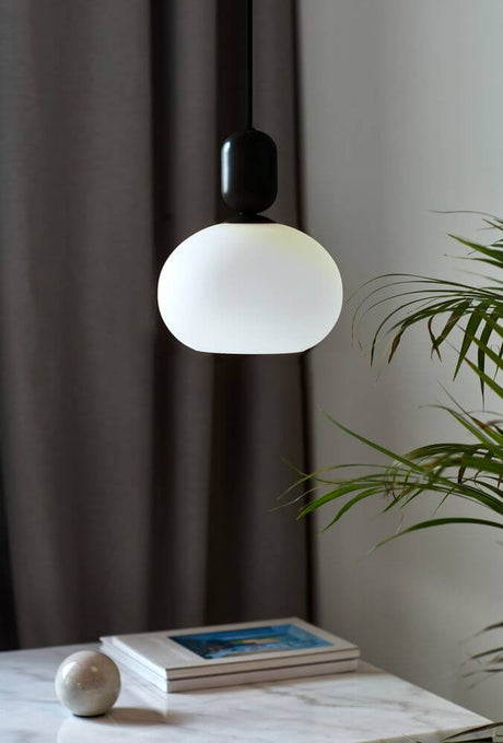 Notti pendel med en kuppelformet opal hvid glasskærm over et bord.
