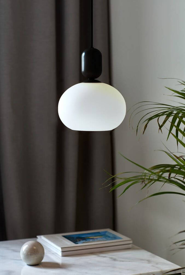 Pendelleuchte Notti mit kuppelförmigem opalweißem Glasschirm über einem Tisch.