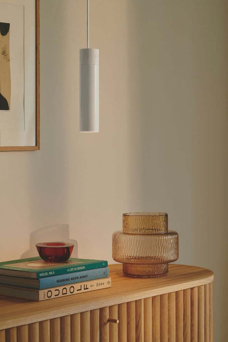 Pendelleuchte Tilo über stilvollem Sideboard mit dekorativen Gläsern und Büchern.