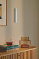 Pendelleuchte Tilo über stilvollem Sideboard mit dekorativen Gläsern und Büchern.