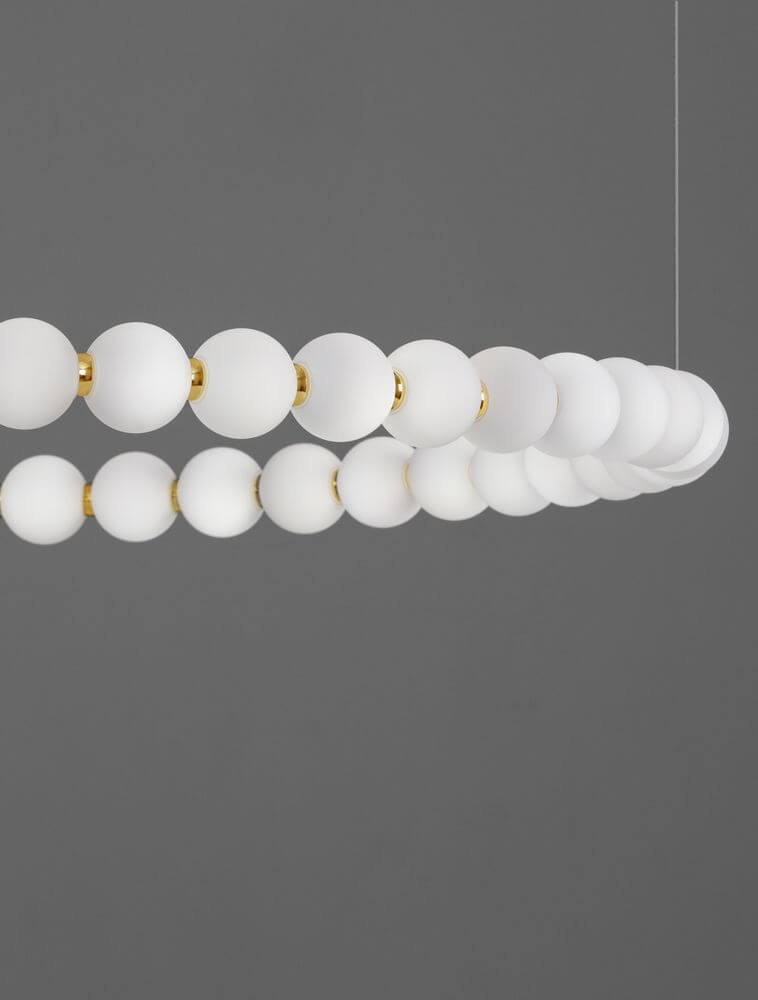 Perla LED Pendelleuchte 46-flammig Ø 104cm 3000K Gold mit goldenen und weißen Kugeln auf grauem Hintergrund.