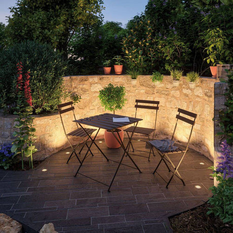 Plug & Shine Bodeneinbaustrahler Floor Mini IP65 95lm 3000K Edelstahl beleuchtet einen Gartentisch in einem Außenbereich.