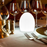 Aida Akku LED-Tischlampe mit stimmungsvollem Licht auf elegant gedecktem Tisch.