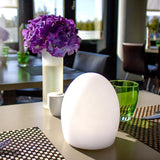 Akku LED-Tischlampe Point Aida auf einem eleganten Tisch mit Blumen und Gläsern im Hintergrund.