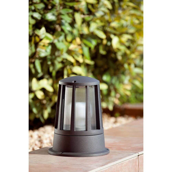 Borne lumineuse moderne SURAT IP54 gris foncé dans le jardin à côté de plantes vertes