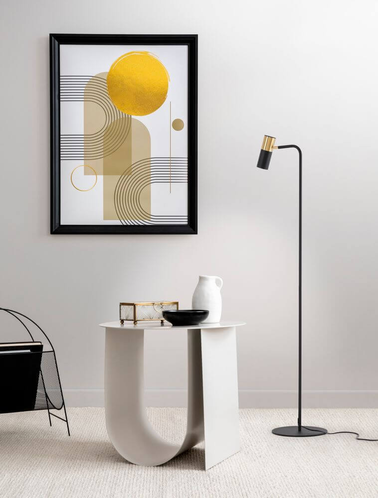 Pongo Stehlampe Schwarz, Gold neben modernem Tisch und Wandkunst mit gelbem Akzent.
