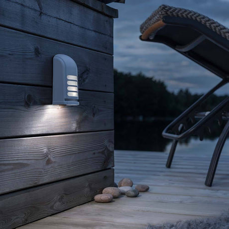 Prato Bateria LED de parede com sensor de movimento 12V Branco numa parede de madeira no exterior à noite.