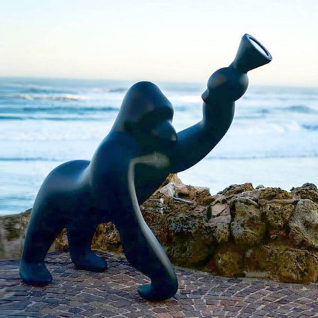 Kong XL floor lamp gorilla in black on the beach with the sea in the background and the lamp arm raised.