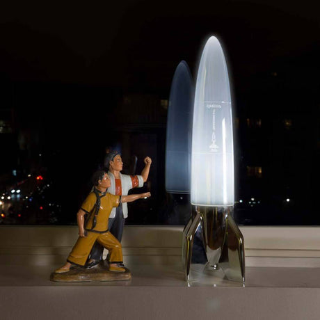 V-2 Schneider rocket table lamp beside a statue of two figures on a windowsill.
