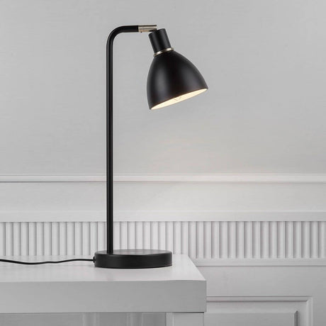 Lampe de table Ray noire sur une table, diffusant une lumière douce pour une utilisation polyvalente.