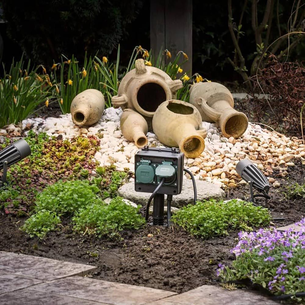 Gartensteckdose IP44 im Garten mit Töpfen und Pflanzen, 1,4m Zuleitung sichtbar, ideal für Außenanschlüsse.