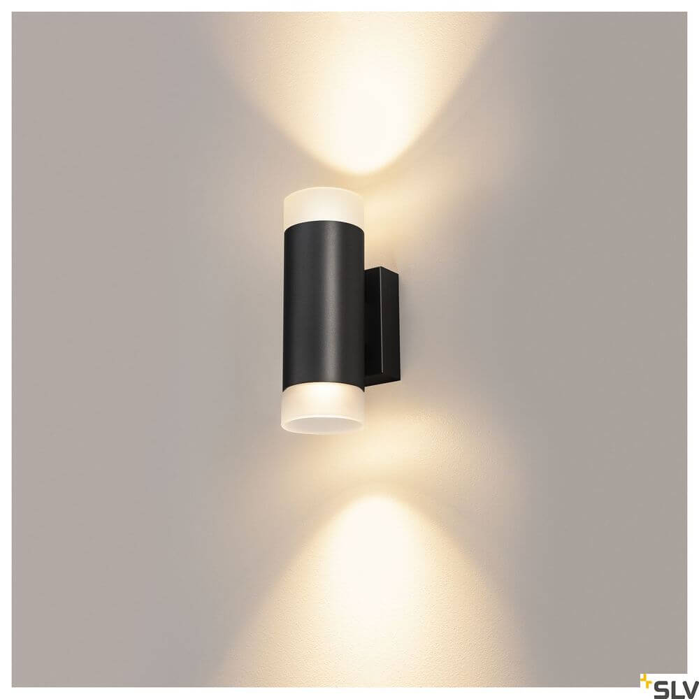 Astina Wandlampe QPAR51 Up & Down Schwarz an einer Wand mit sanftem Licht.