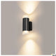 Astina Wandlampe QPAR51 Up & Down Schwarz an einer Wand mit sanftem Licht.