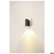 Enola LED applique murale Round S Single Outdoor anthracite montée sur un mur, éclairée d’une lumière chaude.