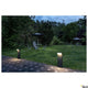 L-Line LED Pollerleuchte Pole Anthrazit CCT IP65 leuchtet Gartenweg bei Nacht, umgeben von Stühlen und Sonnenschirm.
