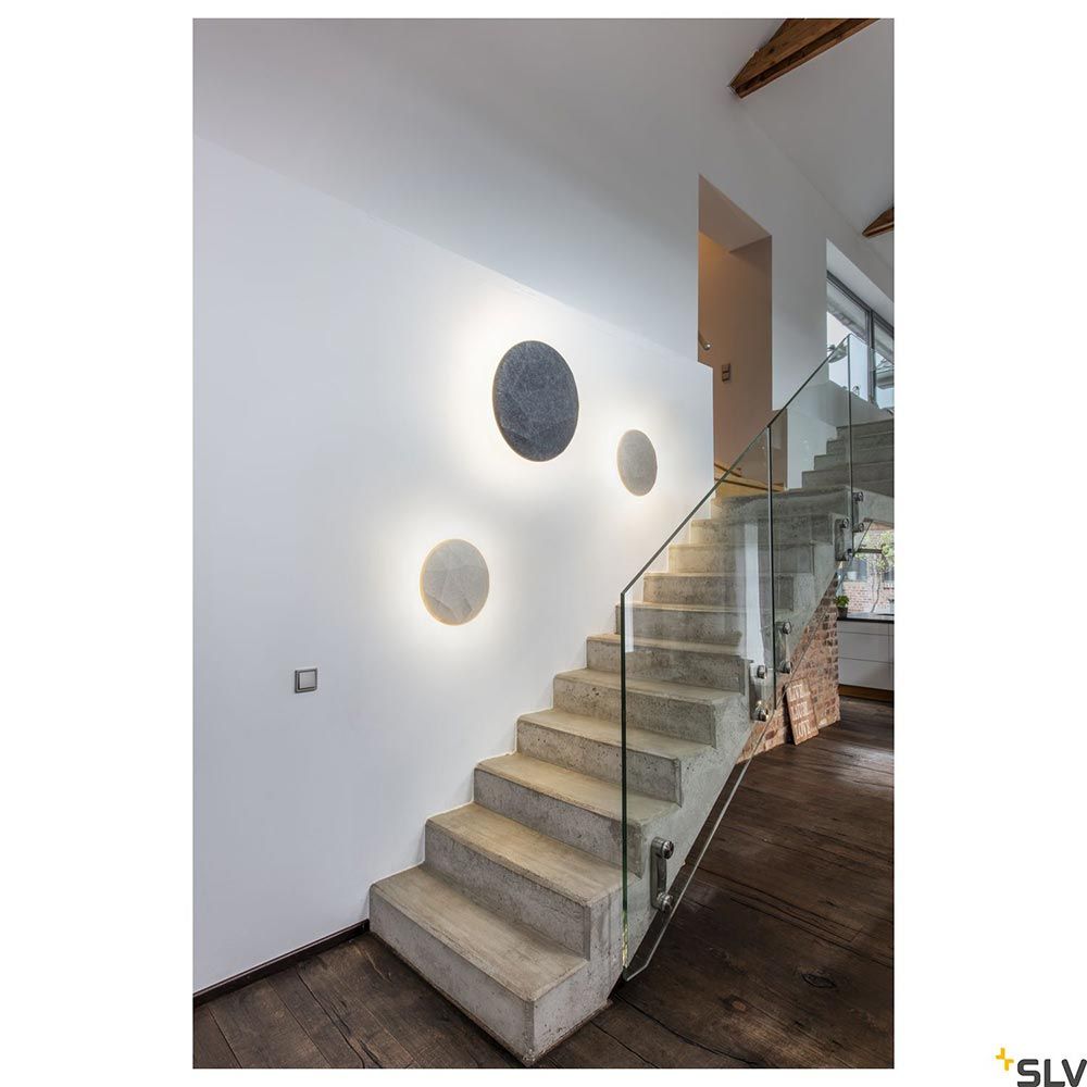 Dimmbare Mana Basis LED Wandaufbauleuchte rund in Anthrazit an einer Treppe mit Lichtkranz-Effekt.