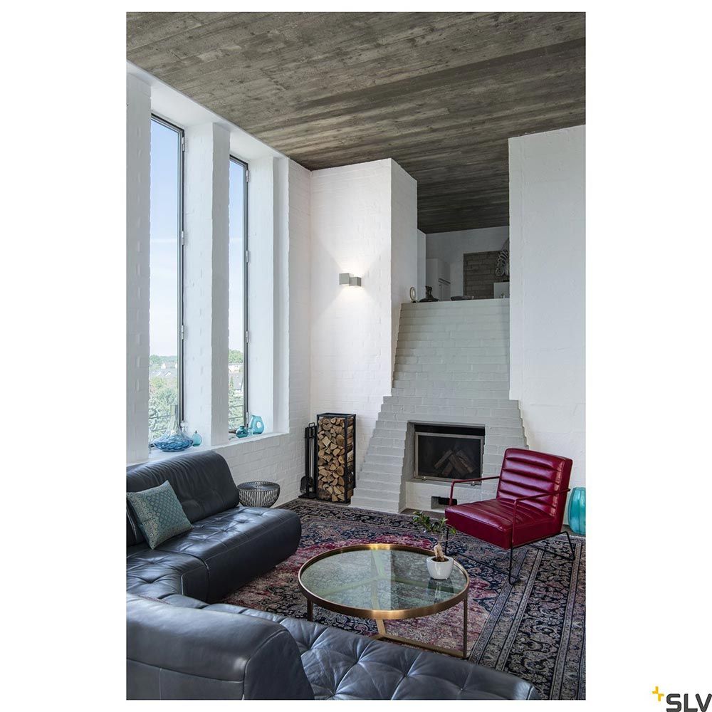 Moderne Wohnlandschaft mit Plastra Wandleuchte in weiß und rotem Sessel in einem hellen Raum.