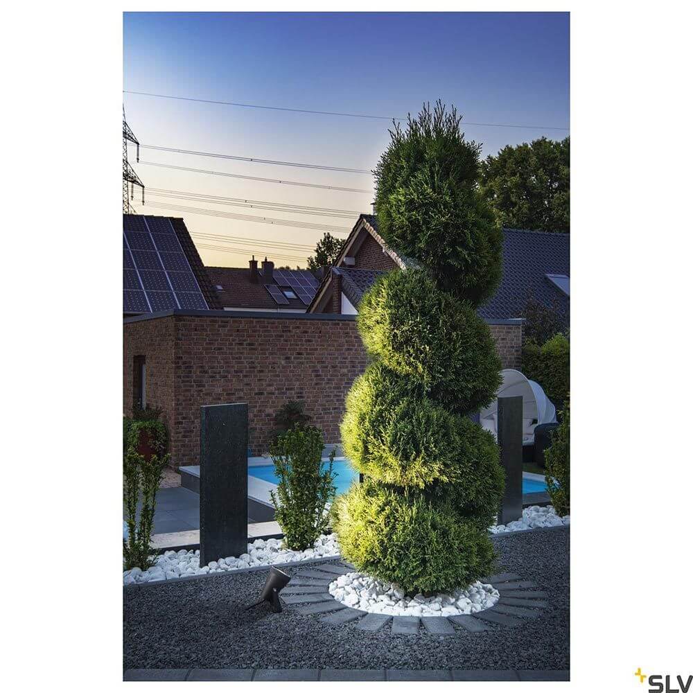 Samrina Single Outdoor Erdspießleuchte Schwarz beleuchtet mit grünem Garten im Hintergrund.