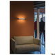 Sedo 7 Wandlampe 3000K Weiß an einer Wand über einem beigen Sofa, moderne Innenraumbeleuchtung.