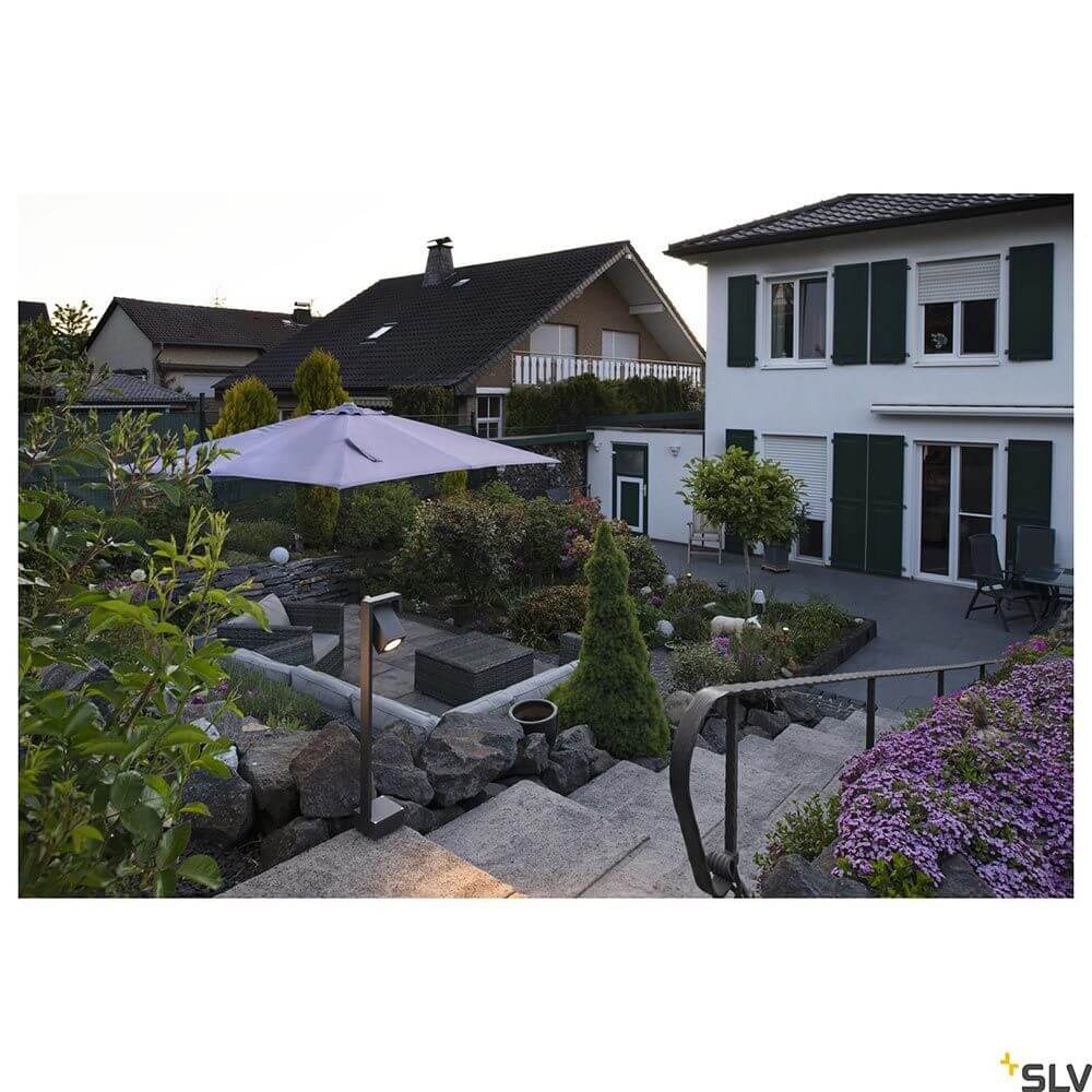Theo Bracket Outdoor Stehleuchte Anthrazit IP65 im Garten mit Sonnenschirm und stilvoller Bepflanzung.
