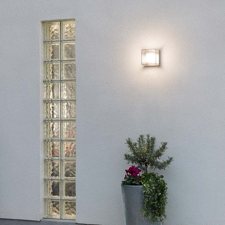 Lampa ścienna LED Sanremo w kolorze szarym zamontowana na ścianie obok donicy z roślinami.