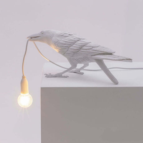 Lampe de table d’extérieur Seletti Bird inclinée avec corbeau et ampoule sur une table.