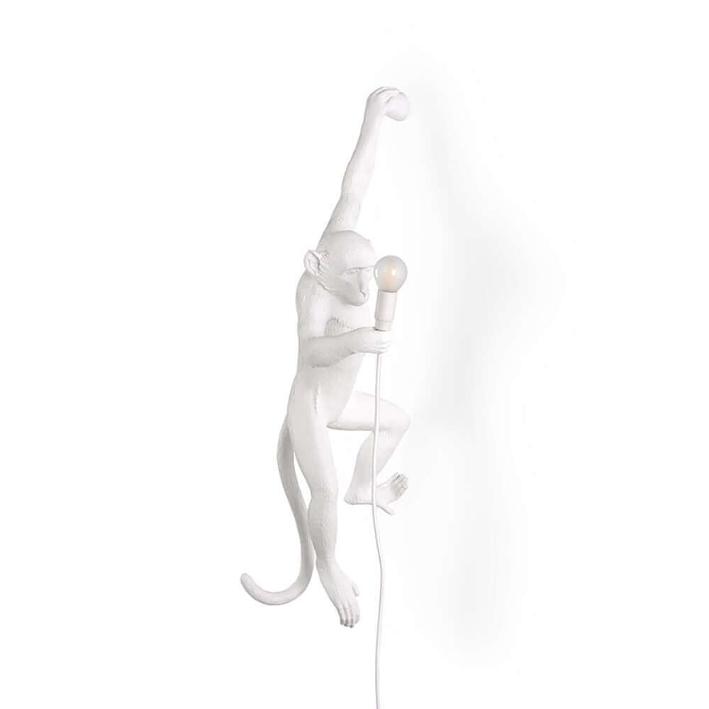 Seletti Monkey Außen-Wandleuchte hängend linke Hand mit weißem Affen, der eine Glühbirne hält.