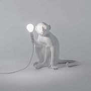 Lampe de table Seletti Monkey assise blanche avec design tigre-singe et lampe lumineuse à la main.