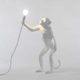 Seletti Monkey Tischlampe stehend Weiß: weiße Lampenfigur eines Affen mit Glühbirne in der Hand.