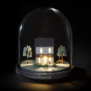 Seletti Min lille nabo LED Bordlampe, der oplyser et lille hus under en glaskuppel om natten.