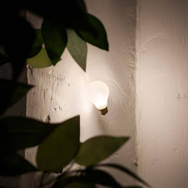Slamp recessed wall lamp light bulb Idea Applique White on a wall with plants in the foreground.