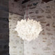 Slamp Pendelleuchte Veli Foliage Weiß in skulpturalem Design, aufgehängt in einem Raum mit Steinwand.