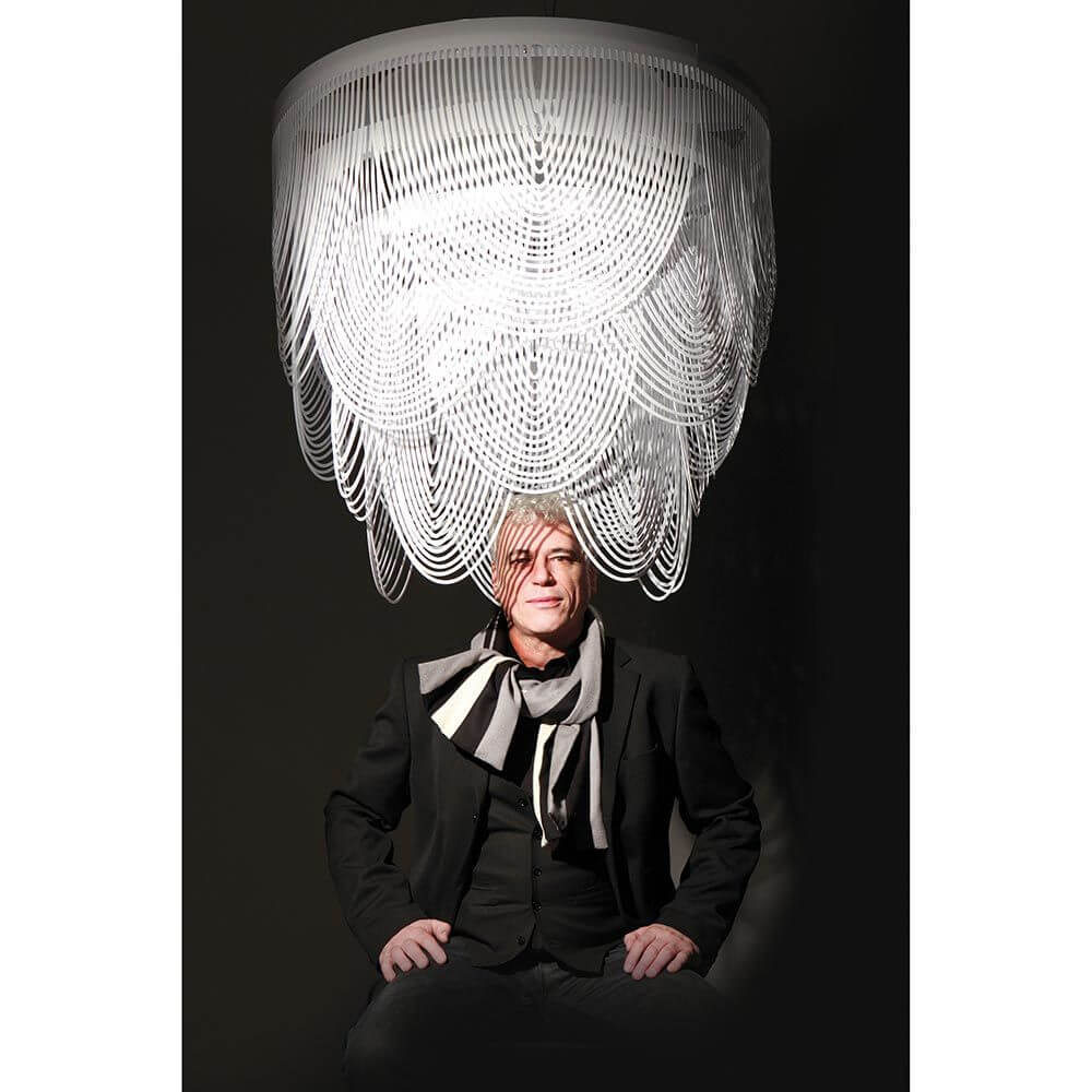 Slamp Hängeleuchte Ceremony Large Weiß über einem Mann mit modischem Look, der in dunklem Raum sitzt.