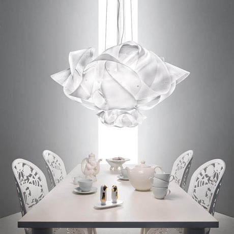 Lampada a sospensione Slamp Fabula Large Prisma Trasparente sopra un elegante tavolo da pranzo con sedie bianche e stoviglie.
