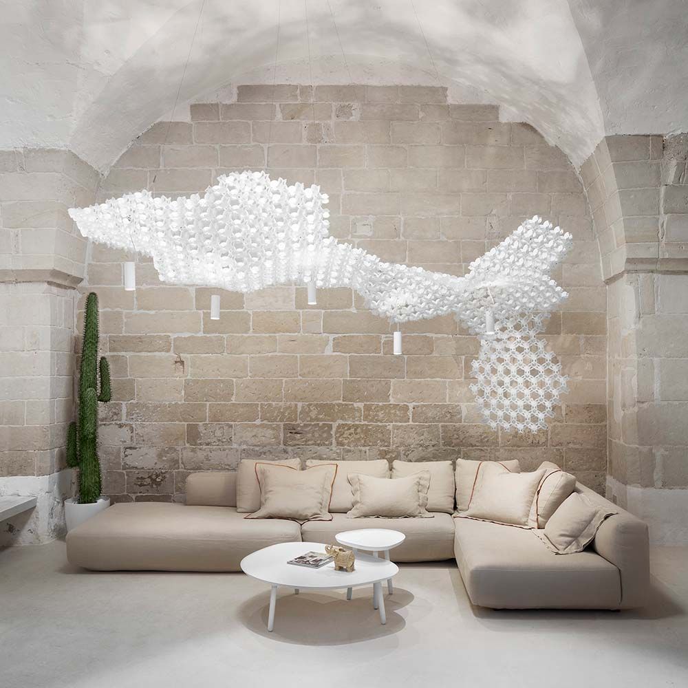 Slamp Nuvem hängendes Lichtobjekt über modernem Sofa in stilvollem Raum mit Steinmauer.