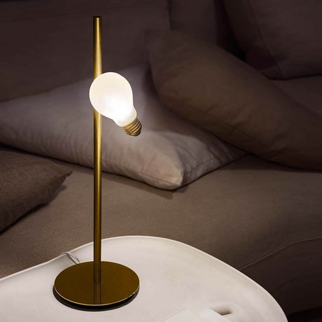 Slamp Tischlampe Idea mit Glühbirne LED Messing-matt auf einem Tisch, Licht leuchtet im Hintergrund.