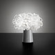 Slamp Tischleuchte Clizia Weiß mit Akku auf einem Tisch, design inspiriert von natürlichen Formen und Lichtreflexionen.