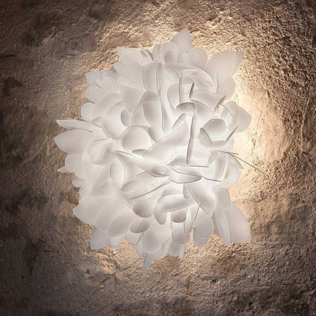 Slamp Wand- & Deckenlampe Veli Foliage mit sanften, schimmernden Formen auf einem rustikalen Hintergrund.