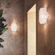 Slamp Wandlampe Charlotte Applique Weiß an einer Wand, mit wabenförmiger Struktur, die warmes Licht erzeugt.