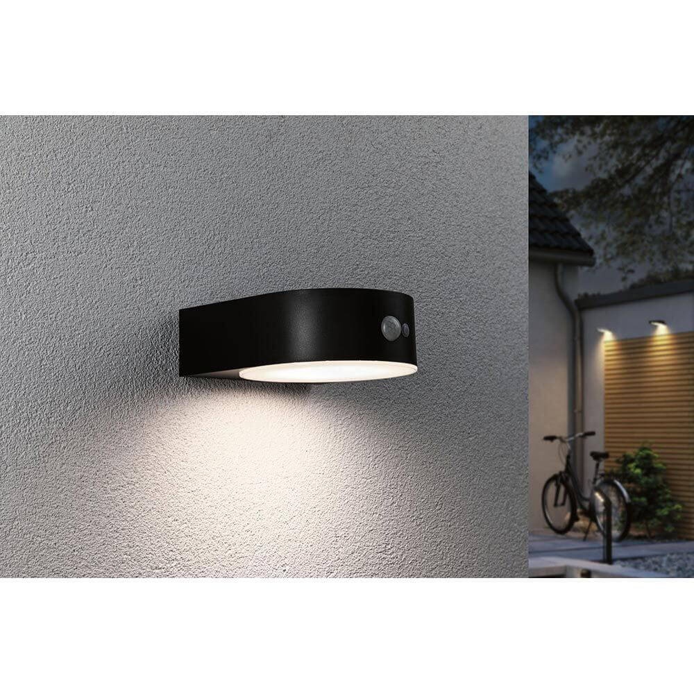 Solar LED Außenwandleuchte Eileen Sensor Schwarz an einer Wand montiert mit warmweißem Licht.